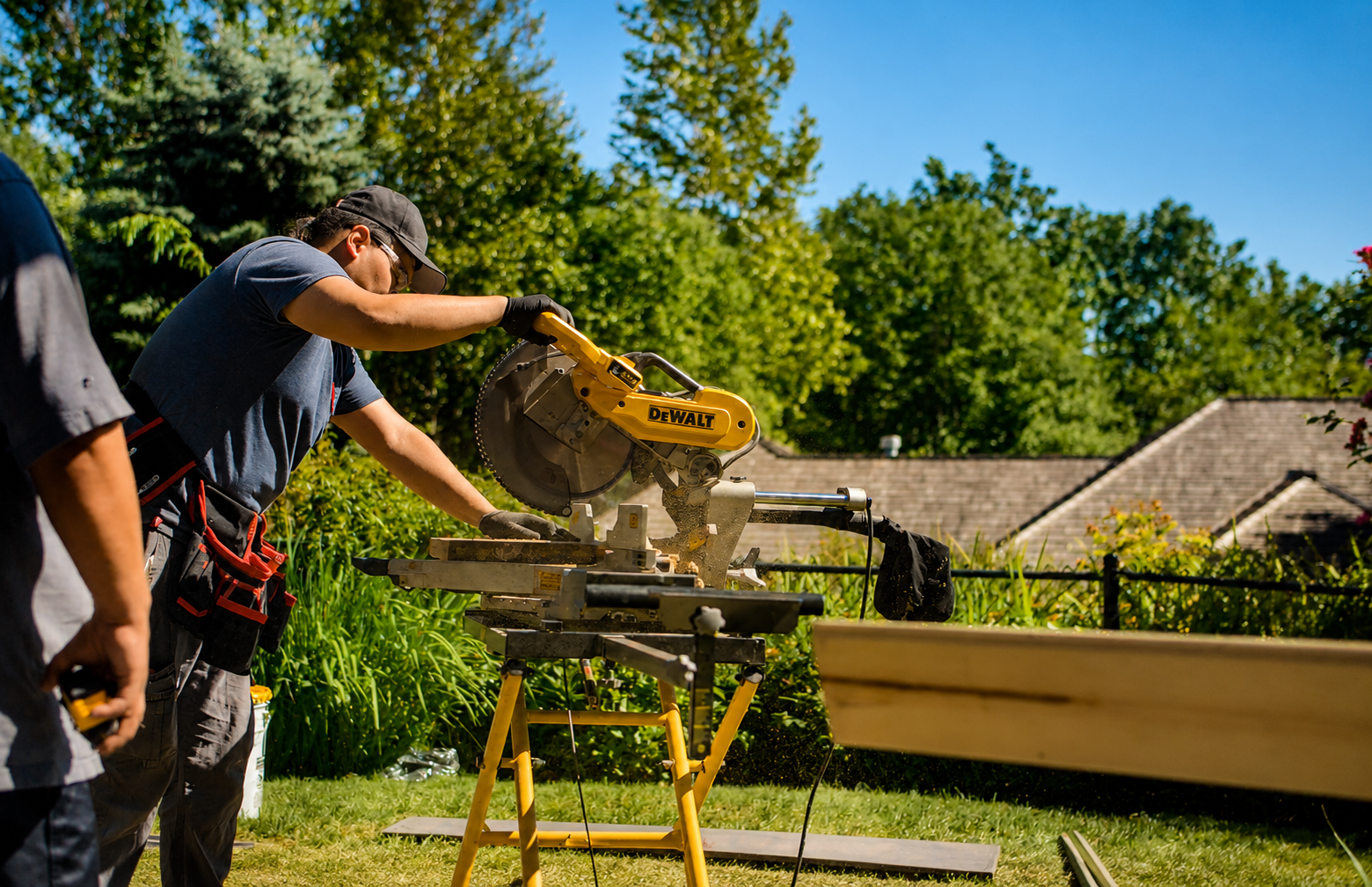 Deck builder in safety glasses using a DeWalt miter saw to cut decking lumber on a jobsite